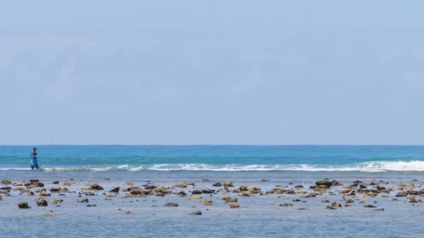 Un pescador vadea en las aguas poco profundas como una lancha rápida pasa en el fondo — Vídeos de Stock