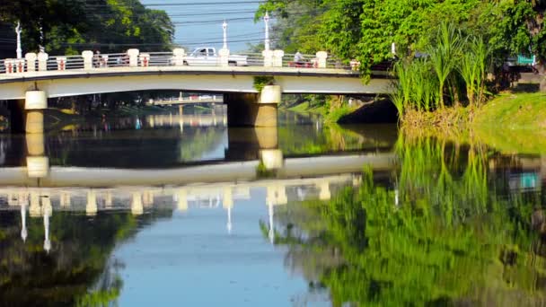 Siem Reap. Kambodja-circa dec 2013: bilar och motorcyklar korsar en bro över en kanal i Siem Reap. Kambodja. Klart vatten återspeglar en spegelbild av himlen och bron. — Stockvideo