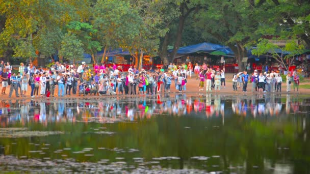 Angkor. Kamboçya - Circa Aralık 2013: Kamboçya'da bir gölet kenarında duran renkli giyimli turistlerin büyük bir kalabalık. Angkor Wat tapınağının fotoğraflarını çekmek. — Stok video