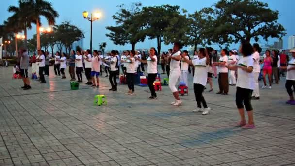 PHNOM PENH. CAMBODIA - CIRCA DIC 2013: Oblique. tiro de gran angular de un hombre camboyano liderando a un gran grupo de mujeres en el baile aeróbico al amanecer en un parque frente al mar en Phnom Penh . — Vídeo de stock