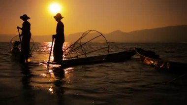 Gün batımında balıkçıların siluetleri. Vintage tekneler ve balık tuzakları. Inle Gölü. Myanmar