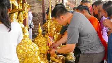 Tayland'daki Ayutthaya Tarih Parkı'ndaki bir tapınakta Buda'nın ve saygı lı keşişlerin heykellerine bastırarak altın yaprak hediye eden Budistler.