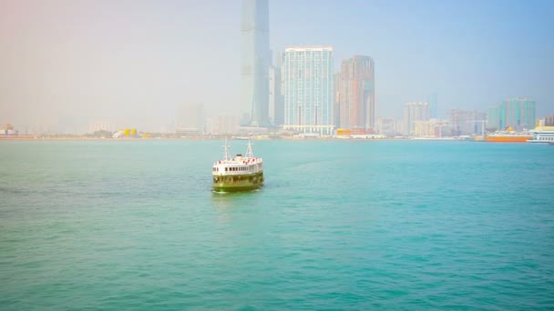 Green and white passenger ferry approaching the pier with the Hong Kong skyline in the background. — Stock Video