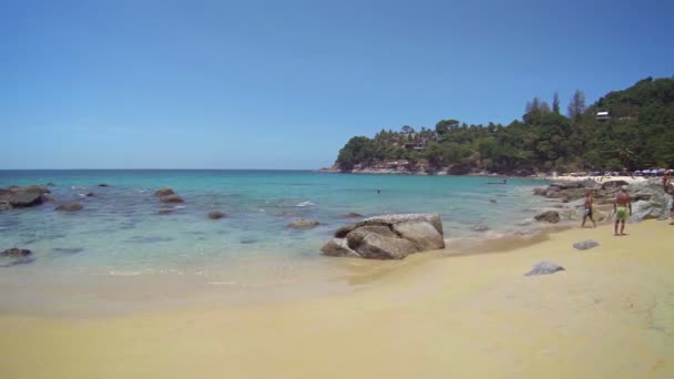 Tourists enjoying the warm tropical waters or cooling themselves in the shade of mature. wild trees at Laem Sing Beach on the island of Phuket in southern Thailand. — Stock Video