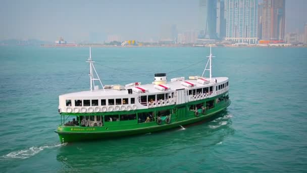 Green and white ferry. called the Morning Star. cruises in Victoria Harbor with a load of passengers. with Hong Kong's skyline in the background. — Stock Video