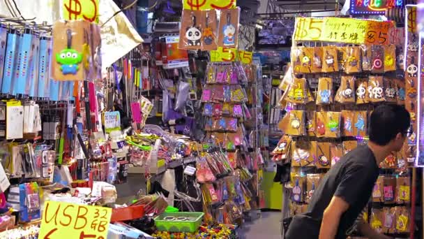 Los compradores navegan por las mercancías de una tienda local de suministros de artesanía en un mercado público local mientras un trabajador reabastece la mercancía — Vídeos de Stock