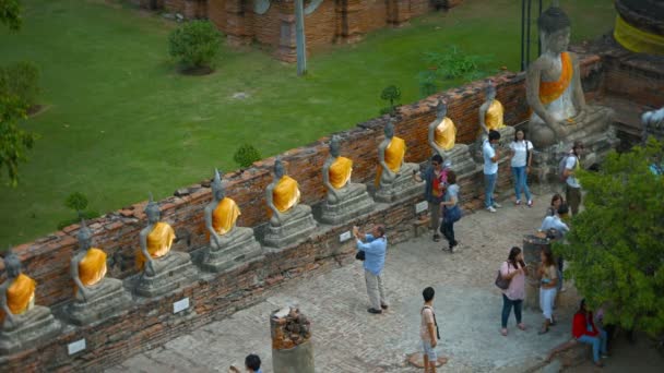 Een rij van identieke boeddhabeelden. gedrapeerd in gele stof. langs een oude muur buiten Wat Yai Chai Mongkhon. een historische tempel in Ayutthaya historisch park — Stockvideo