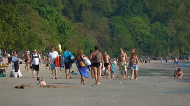 Счастливые туристы толпа популярных Railay Beach с его красивым лесистым склоном холма и известняковых скал на заднем плане . — стоковое видео