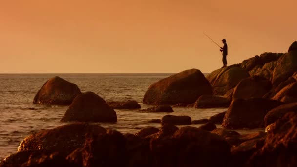 KAMALA. PHUKET. THAILAND - CIRCA DEC 2014: Silhouette of angler. fishing from the rocks at sunset. with open sea and horizon in the background. — Stock Video