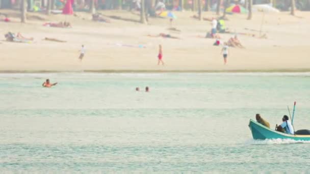 カマラ。プーケット。タイ - 2014年12月頃:小さなフレームを横切る地元の漁師。手作り。観光客が砂浜で遊ぶ木製のボート. — ストック動画