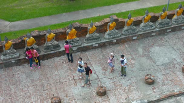 아유타야. 태국 - Circa 2015: 태국 아유타이 역사 공원의 왓 야이 차이 몽콘에서 동일한 부처님 조각의 행을 보고 관광객의 그룹. — 비디오