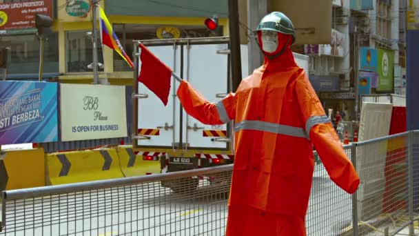Un maniquí de seguridad. vestida con ropa naranja brillante. ondeando una bandera roja de precaución con su brazo mecánico. en un sitio de construcción en el centro de Kuala Lumpur. Malasia . — Vídeos de Stock