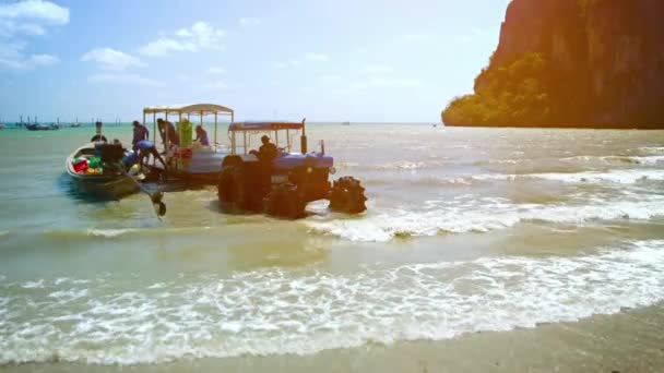 Arbeiderne losser last og forsyninger fra en båt på grunt vann. Inn i en trailer. trekkes av en landbrukstraktor til Railay Beach i Thailand . – stockvideo