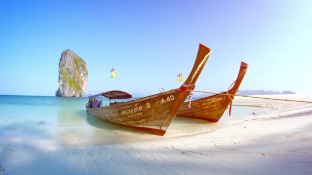 Красиво сделанные длиннохвостые лодки ручной работы. равен в Railay Beach в Таиланде. с большим скальным образованием, вырывающимся из моря на заднем плане . — стоковое видео