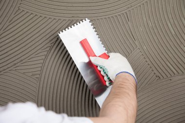 the worker applies glue for a tile on a wall  clipart