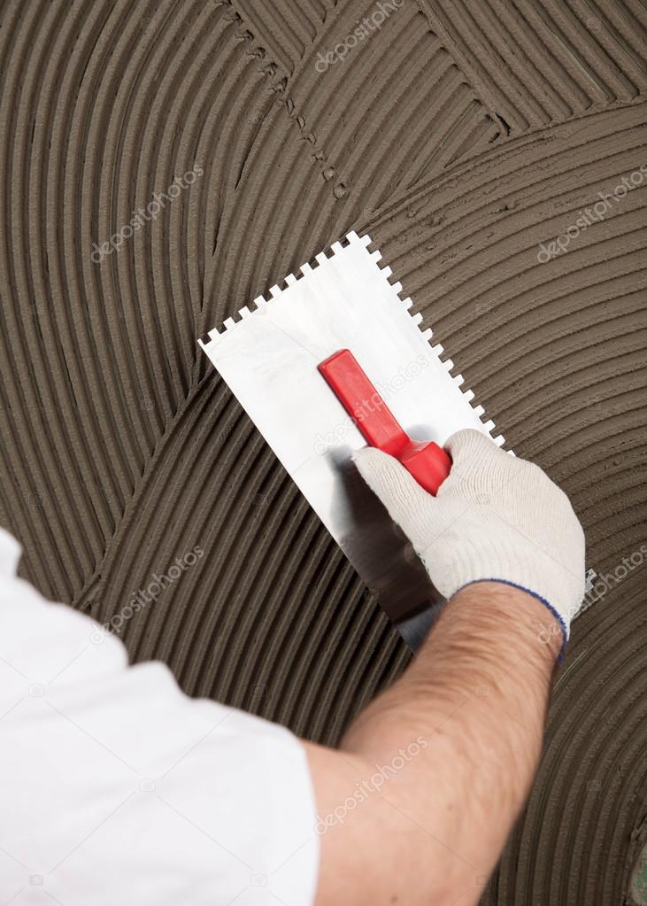 the worker applies glue for a tile on a wall 