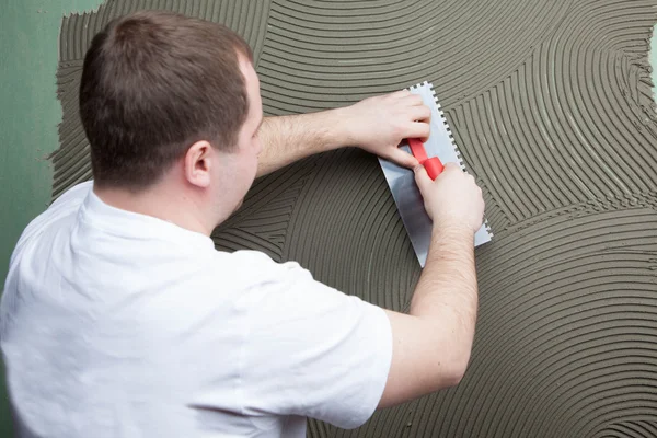 Der Bauarbeiter trägt Leim auf die Wand für die keramische Fliese auf — Stockfoto