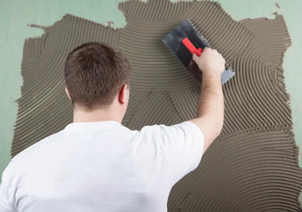 O construtor de trabalho aplica a cola em uma parede de uma telha cerâmica. f) — Fotografia de Stock