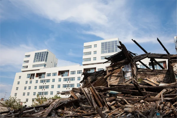 Altes zerstörtes Holzhaus auf dem Hintergrund der neuen Gebäude — Stockfoto