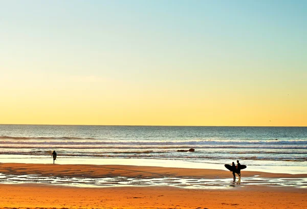 Surfers op oceaan strand bij zonsondergang — Stockfoto