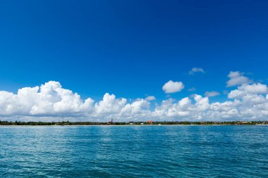 Bulutlar mavi gökyüzünde sakin denizin üzerinde güneş ışığı yansımasıyla