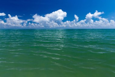 Bulutlar mavi gökyüzünde sakin denizin üzerinde güneş ışığı yansımasıyla