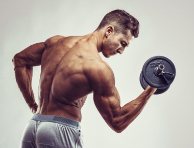 Kaslı vücut geliştirmeci adam ile boşaltmak gri arka plan üzerinde dumbbells ile yapıyor