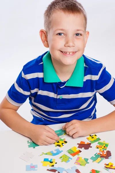 Netter kleiner Junge beim Puzzeln am Tisch Stockbild