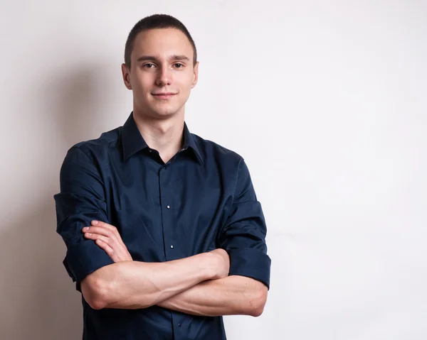 Joyeux jeune homme. Portrait de beau jeune homme en chemise décontractée gardant les bras croisés et souriants tout en se tenant debout sur fond gris — Photo