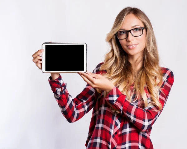 Lässig lächelnde Frau zeigt leeren Tablet-Computer-Bildschirm vor grauem Hintergrund. — Stockfoto