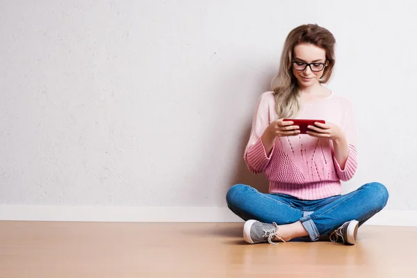 Feliz hermosa mujer sentada en el suelo y utilizando el teléfono inteligente — Foto de Stock