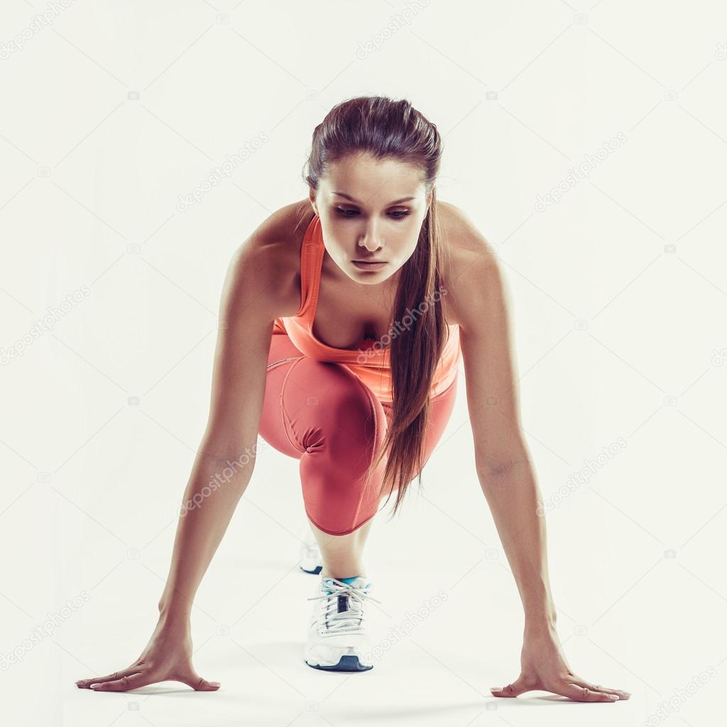Fit female athlete ready to run over grey background. Female fitness model preparing for a sprint