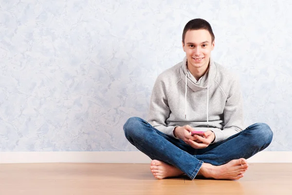Ritratto di un giovane seduto sul pavimento con un cellulare, isolato. pronto per il vostro design — Foto Stock