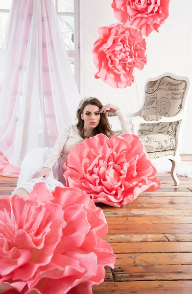 Beautiful sexy girl in a long dress with a huge pink flowers sitting by the window — Stock Photo, Image