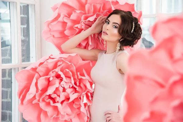 Schöne sexy Mädchen in einem langen Kleid mit einem riesigen rosa Blumen sitzt am Fenster — Stockfoto