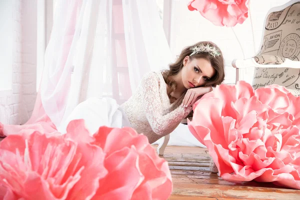 Beautiful sexy girl in a long dress with a huge pink flowers sitting by the window — Stock Photo, Image