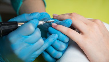 Closeup shot of a woman in a nail salon receiving a manicure by a beautician with nail file. Woman getting nail manicure. Beautician file nails to a customer clipart