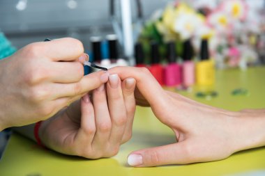 Closeup shot of a woman in a nail salon receiving a manicure by a beautician with nail file. Woman getting nail manicure. Beautician file nails to a customer clipart