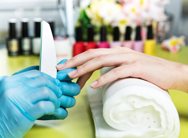 Nahaufnahme einer Frau in einem Nagelstudio, die von einer Kosmetikerin mit Nagelfeile eine Maniküre erhält. Frau bekommt Nagelmaniküre. Kosmetikerin feilt Nägel an Kundin — Stockfoto