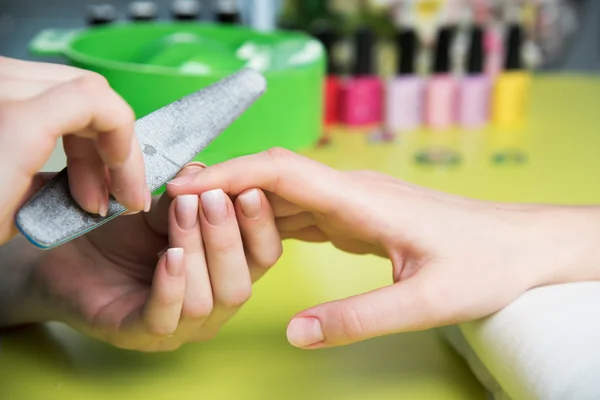 Nahaufnahme einer Frau in einem Nagelstudio, die von einer Kosmetikerin mit Nagelfeile eine Maniküre erhält. Frau bekommt Nagelmaniküre. Kosmetikerin feilt Nägel an Kundin — Stockfoto