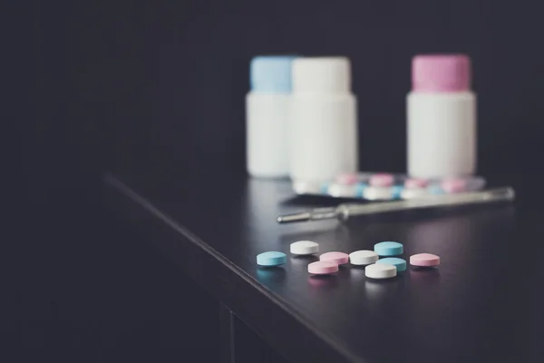 Barevné pilulky a teploměr na hnědý stůl — Stock fotografie