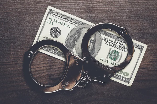 Handcuffs and one hundred dollars on wooden table — Stock Photo, Image