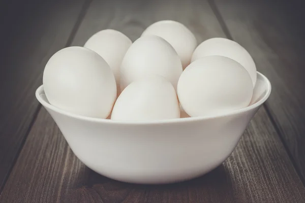 Ovos em tigela branca na mesa de madeira — Fotografia de Stock