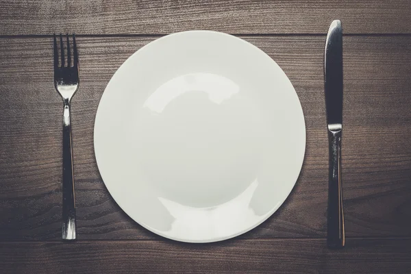 Weißer Teller mit Messer und Gabel auf Holztisch — Stockfoto