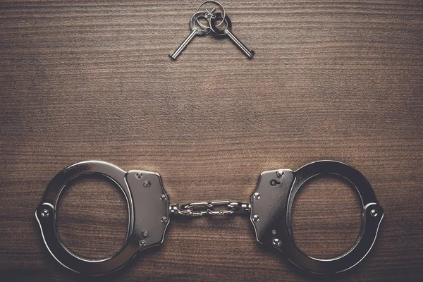 Steel handcuffs and keys on the wooden background — Stock Photo, Image