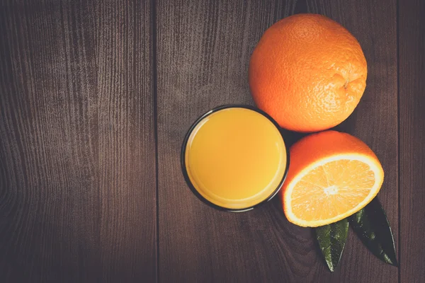Świeżych pomarańczy i szkła z soku na drewniane tła — Zdjęcie stockowe