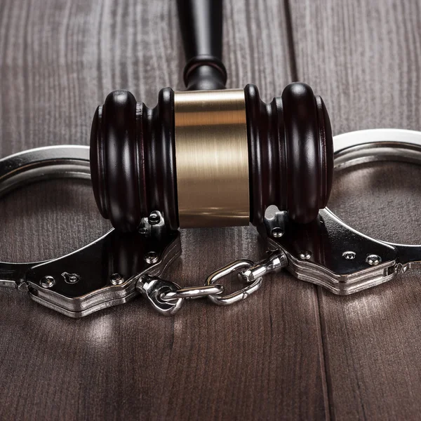 Handcuffs and judge gavel on brown wooden table — Stock Photo, Image