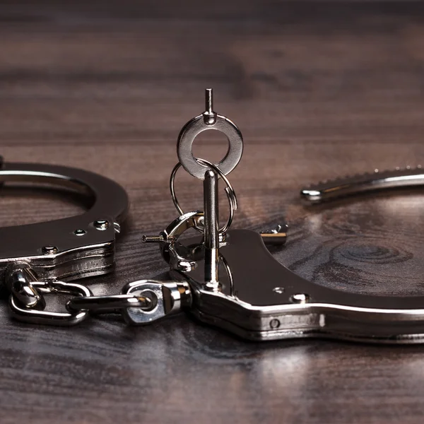 Handcuffs and keys on brown wooden table background — Stock Photo, Image