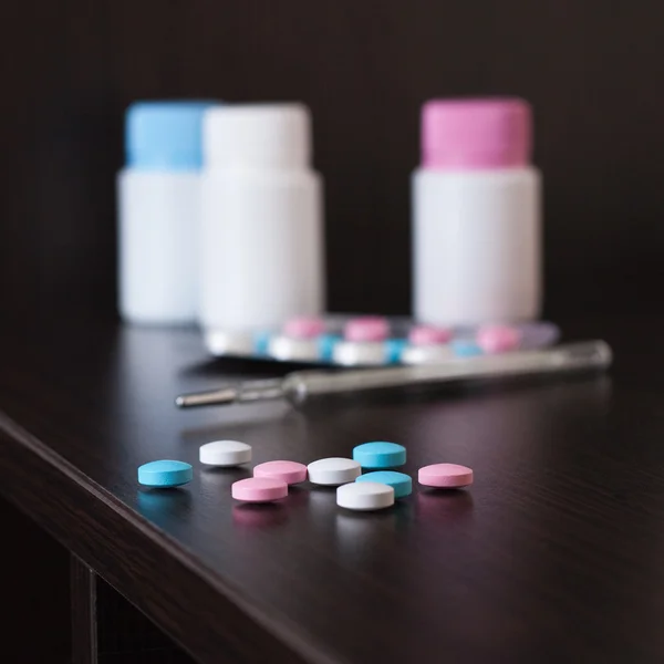 Pilules et thermomètre sur table brune — Photo