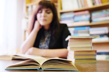 Kız öğrenci bir kitaplıktaki bir kitap okur